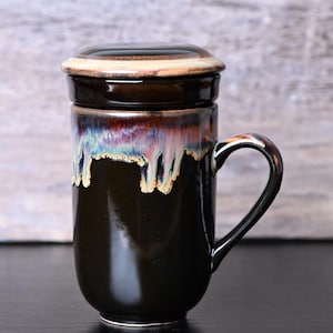 May include: A dark brown ceramic mug with a matching lid. The mug has a handle and a unique glaze that drips down the sides, showcasing iridescent colors. The mug is designed for tea or coffee.