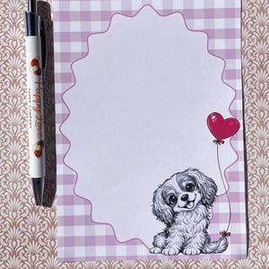 May include: A notepad with a pink gingham border and a scalloped edge. A cartoon puppy with a red heart balloon is on the bottom right. A pen with the text "Puppy Love Paper Company" is on the left.