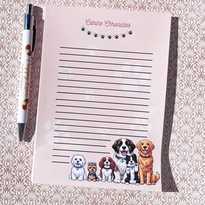 May include: A notepad with the text "Canine Chronicles" and a row of paw prints. The notepad features a line of illustrated dogs at the bottom. A pen with the text "Puppy Love Paper Company" is next to the notepad.