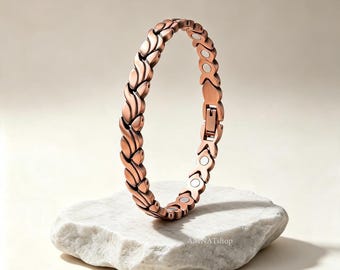 May include: A copper-colored link bracelet featuring a repeating wave-like pattern on the exterior and circular magnetic inserts on the interior. The bracelet includes a secure metal clasp mechanism and displays the text AMNATshop on the surface.