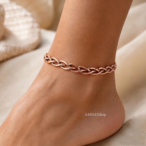 May include: A rose gold anklet featuring a continuous braided chain design. The metal links are interconnected to form a repeating woven pattern that encircles the ankle. The text AMNATshop is visible in the lower right corner of the image.
