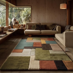 May include: A colorful geometric rug with a patchwork design dominates the foreground. The rug features rectangular blocks in shades of green, orange, blue, brown, and cream. The room has a neutral color palette with wooden walls and a beige sofa.