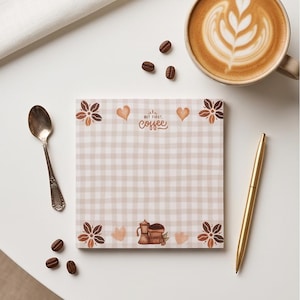 May include: A square notepad featuring a light beige and white gingham pattern. The top center displays the text "BUT FIRST, coffee" in brown script. The corners are decorated with brown coffee bean flowers, and the bottom center shows a moka pot.