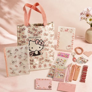 Pode incluir: Um conjunto de papelaria com o tema Hello Kitty, incluindo uma bolsa de lona com alças cor-de-rosa, uma bolsa com fecho, um bloco de notas pautado, um pequeno bloco de notas, autocolantes, um porta-chaves, um elástico e canetas.