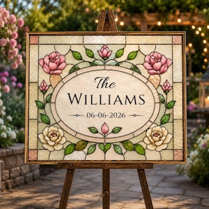 May include: A framed stained glass sign on a wooden easel. The sign features the name "The Williams" and the date "06-06-2026" in an oval frame, surrounded by pink and cream roses and green leaves.