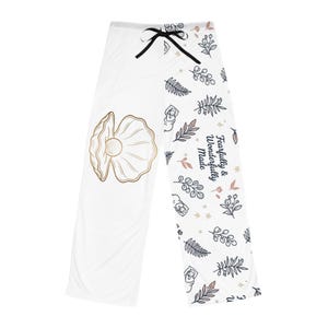 May include: White pajama trousers with a black drawstring and floral pattern. The trousers feature a gold seashell design and the text "Fearfully & Wonderfully Made" in a script font.