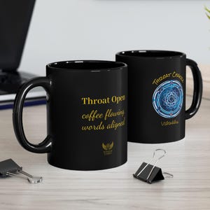May include: Two black ceramic mugs with gold text and a blue and white graphic. One mug reads "Throat Open coffee flowing words aligned." The other mug says "Throat Chakra Vishuddha."
