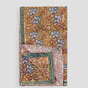 May include: A folded quilt with a floral pattern in gold, blue, red, and green. The quilt displays a repeating design of stylized flowers and leaves. It has a green border. The quilt is folded to show the pattern.