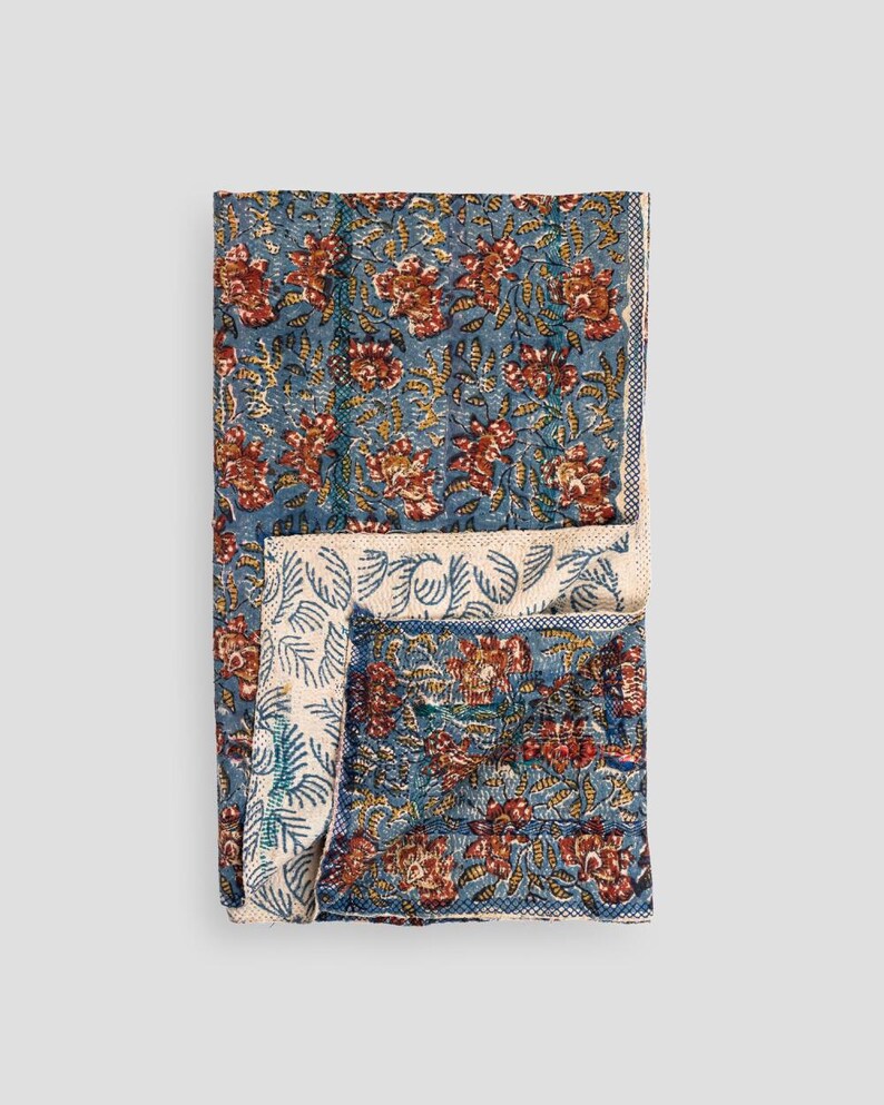 May include: A folded blue floral quilt with a repeating pattern of red and yellow flowers and leaves. The quilt has a white border with a blue leaf pattern. The quilt is made of a soft, comfortable material.