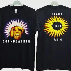 May include: Black t-shirt featuring the band Soundgarden. The front graphic shows a distressed face with a white and purple burst, and the band's name. The back displays a yellow and red sun with the words "Black Hole Sun".