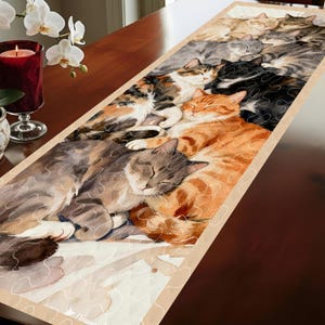 May include: A rectangular table runner featuring a watercolor illustration of several sleeping cats in various colors, including orange, gray, and calico. The runner has a beige border and a quilted design.