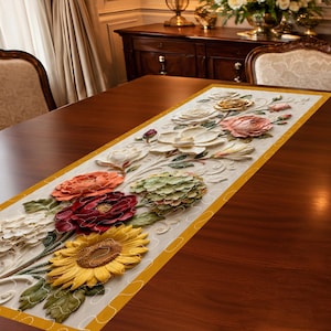 May include: A floral table runner featuring a variety of colorful, three-dimensional flowers. The runner has a cream-colored background with a yellow border. The flowers include a sunflower, roses, and other blooms in shades of red, orange, and yellow.