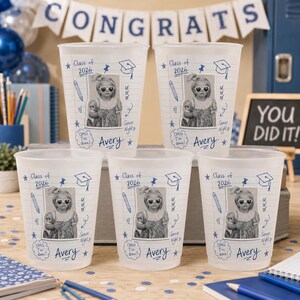 May include: Five clear plastic cups with a graduation theme. Each cup features a photo of a person wearing sunglasses, the text "Class of 2026", and the name "Avery". The cups are decorated with blue drawings of pencils, stars, and graduation caps.