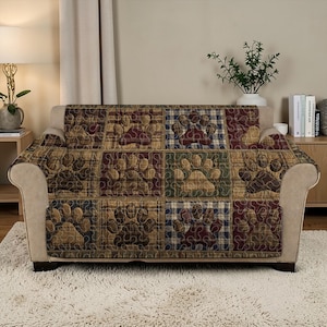 May include: A quilted sofa cover featuring a patchwork design with paw prints. The cover has a plaid pattern in shades of brown, red, blue, and green. The paw prints are in a contrasting tan color, adding a decorative touch to the furniture.