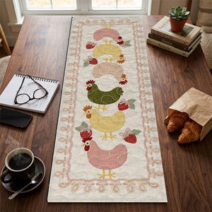 May include: A cream-colored quilted table runner featuring a repeating pattern of colorful chickens and strawberries. The chickens are in shades of pink, yellow, and green, with red combs and beaks. The runner is bordered with a pink lace design.