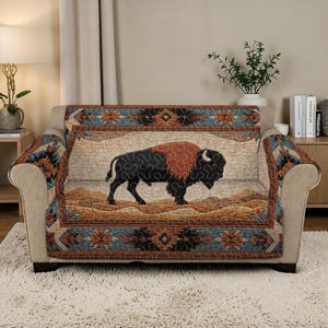 May include: A beige sofa with a decorative cover featuring a bison design. The cover has a southwestern pattern in shades of brown, blue, and orange. The bison is black with a reddish-brown mane, set against a landscape.
