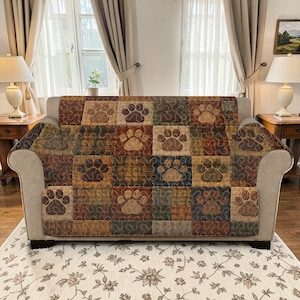 Puede incluir: Una funda de sofá estampada con un diseño de patchwork con huellas de patas en tonos marrón, beige y verde. La funda está colocada sobre un sofá beige en una habitación con cortinas y lámparas.