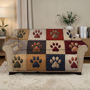 Puede incluir: Una funda de sofá de retazos con un patrón repetido de huellas de patas. La funda está hecha de cuadrados en varios colores, incluyendo beige, rojo y azul. Las huellas de patas son en tonos marrones y beige.
