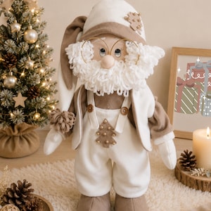 Pode incluir: Boneca Boho Chic Papai Noel feita à mão com barba branca, óculos e chapéu a condizer. A boneca usa uma roupa branca com detalhes em castanho e uma pequena aplicação de árvore de Natal. A imagem inclui o texto "PDF Pattern".