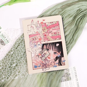 Könnte beinhalten: Ein beiges Notizbuch mit einer Illustration im Manga-Stil. Das Kunstwerk zeigt ein Mädchen, das eine Kassette hält, sowie rosa Kassetten und Cartoonfiguren. Die Worte "You're My Only" sind sichtbar.
