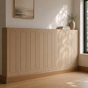 May include: A long, low-profile storage cabinet featuring eight vertical doors with a light tan, matte finish. Each door is accented with a recessed, elongated octagonal panel design. The unit sits flush against a wall, providing a clean, uniform look.