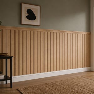 May include: A wall featuring light brown vertical beadboard paneling with a matching chair rail molding. The upper wall is painted a muted sage green, and a framed square art piece with a black abstract shape hangs on the wall above the paneling.
