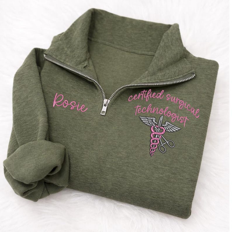 May include: Olive green quarter-zip sweatshirt with the name "Rosie" embroidered in pink on the left chest. The right chest features a pink and gray medical symbol with the words "certified surgical technologist".
