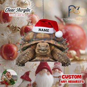 May include: A clear acrylic 2D flat hanging ornament featuring a brown tortoise wearing a red and white Santa hat with the text NAME printed on the brim. The tortoise is wrapped in colorful Christmas string lights. A 4mm thickness is shown.