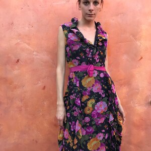 May include: A sleeveless maxi dress with a floral print in shades of pink, orange, and yellow on a black background. The dress has a ruffled neckline and a pink belt.