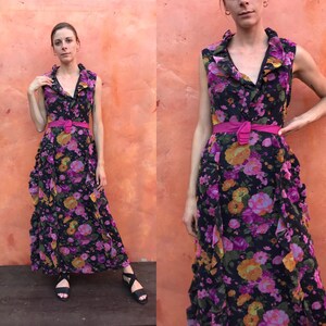 May include: A long, black maxi dress with a floral print in shades of pink, orange, and yellow. The dress has a ruffled neckline and a pink belt.