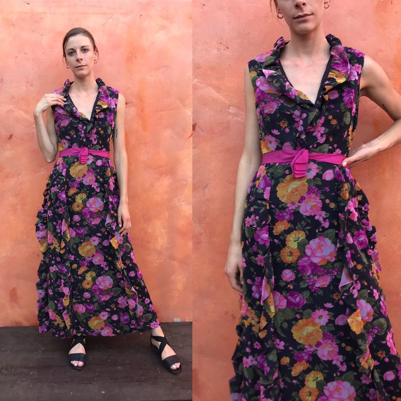 May include: A long, black maxi dress with a floral print in shades of pink, orange, and yellow. The dress has a ruffled neckline and a pink belt.