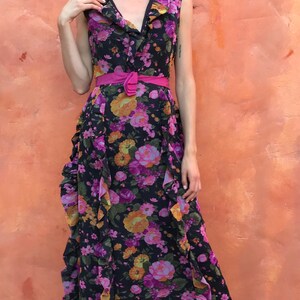 May include: A woman wearing a long, black floral dress with a pink ruffled collar and a pink belt. She is wearing black sandals with straps.