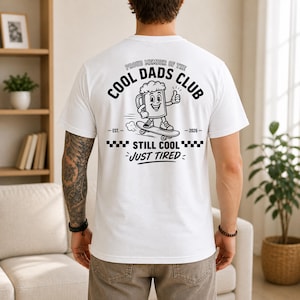 May include: White t-shirt with a graphic on the back that reads "Proud Member of the Cool Dads Club." The graphic features a beer mug on a skateboard with the text "Still Cool, Just Tired."