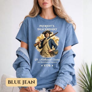 Puede incluir: Camiseta azul con el texto "PATRIOT'S DESCENDANT" y una ilustraci&oacute;n de un hombre con uniforme colonial sosteniendo un rifle. El texto "Lt. Nathaniel Carter 2nd Massachusetts Regiment" y el a&ntilde;o "1776" tambi&eacute;n est&aacute;n impresos.