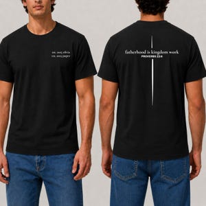 May include: Black t-shirt with white text on the front and back. The front reads "est. 2025 olivia" and "est. 2023 jasper." The back of the shirt says "fatherhood is kingdom work PROVERBS 22:6" with a vertical line design.