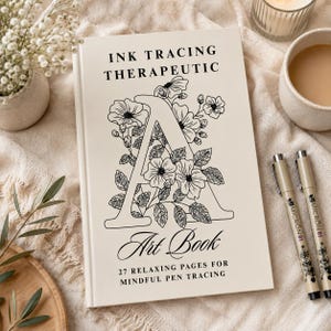 Könnte beinhalten: Ein cremefarbenes Buch mit dem Titel INK TRACING THERAPEUTIC und einem großen schwarzen Buchstaben A in Strichzeichnung, der mit Blumenillustrationen verziert ist. Das Cover enthält den Text Art Book und 27 RELAXING PAGES FOR MINDFUL PEN TRACING.