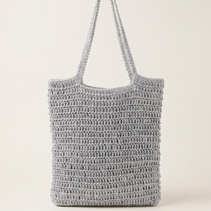 May include: A silver-colored tote bag crafted with a textured, open-weave crochet pattern. The bag features a rectangular body and two integrated shoulder straps, showcasing a consistent metallic finish throughout the entire crocheted construction.