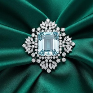 May include: A luxurious brooch featuring a large, rectangular, light blue gemstone at its center, surrounded by smaller, sparkling white gemstones. The brooch is set against a backdrop of deep emerald green satin fabric.