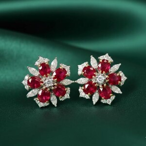 Può includere: Un paio di orecchini a forma di fiore. Ogni orecchino presenta un gruppo centrale di piccoli diamanti rotondi circondati da sei pietre preziose ovali rosso scuro. I petali sono delineati da piccoli diamanti trasparenti, su metallo dorato.