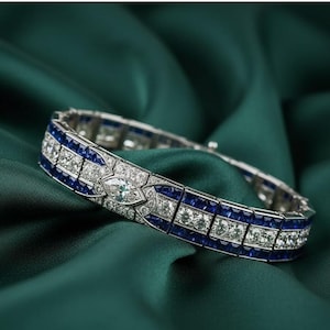 Könnte beinhalten: Ein silbernes Armband mit geometrischem Design, das abwechselnd blaue Edelsteine und klare, funkelnde Steine aufweist. Das Armband ist vor einem dunkelgrünen, seidigen Hintergrund platziert, der seine komplizierten Details und sein luxuriöses Aussehen hervorhebt.
