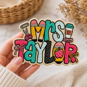 May include: Embroidered patch with the text "Mrs. Taylor" in colorful letters, featuring school-themed icons like pencils, scissors, and a coffee cup. The patch has a beige background and a pink border.
