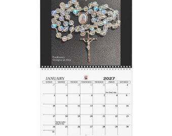 May include: A 2027 wall calendar for January featuring a rosary with iridescent, translucent beads, a central oval medal depicting a figure, and a silver-toned crucifix. The text FoxRosary Designs on Etsy is printed in the lower left corner.