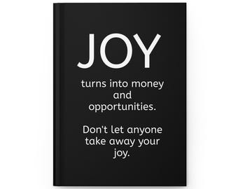 May include: A black journal with the word "JOY" in large white letters at the top. Below, the text reads "turns into money and opportunities. Don't let anyone take away your joy." The journal is closed and has a clean, minimalist design.