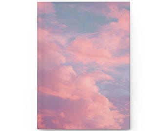 May include: A hardcover journal featuring a dreamy sky design. The cover displays a soft, pastel color palette of pink and blue clouds. The journal is rectangular and has a clean, minimalist aesthetic.