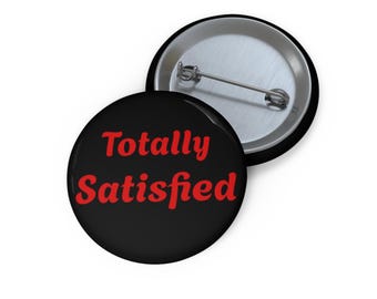 May include: Black button with the words "Totally Satisfied" in red, with a pin back. Another button is partially visible, showing the pin back and a black rim.