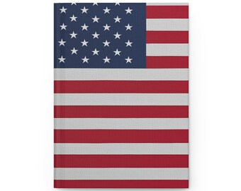 May include: A hardcover journal featuring the American flag design. The cover displays the iconic red and white stripes and a blue field with white stars. The journal is rectangular and appears to be made of a textured material.