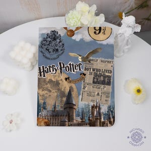 May include: A decorative Harry Potter-themed notebook featuring the Hogwarts crest, a golden snitch, and an owl. The cover includes the text "Harry Potter" and a newspaper clipping. The background is a collage of castle illustrations.