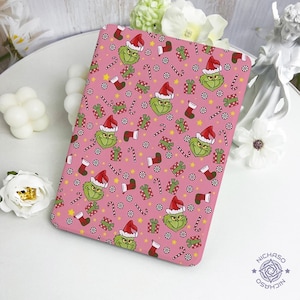 May include: A pink rectangular item featuring a repeating pattern of a green character wearing a Santa hat, Christmas stockings, wrapped gifts, candy canes, and snowflakes. The design is festive and holiday-themed.