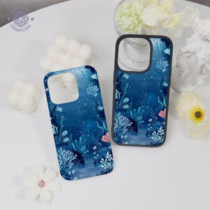 May include: Two phone cases with a dark blue underwater design featuring coral, seaweed, and small fish. The cases have a black border and a glossy finish. The design includes white, teal, and pink accents, creating a vibrant ocean theme.