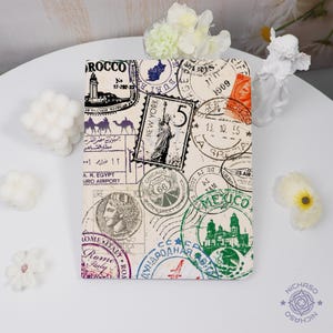 May include: A cream-coloured notebook cover with a collage of vintage stamps and travel imagery. The design includes stamps from New York, Mexico, and Rome, with text in multiple languages. The cover is rectangular.